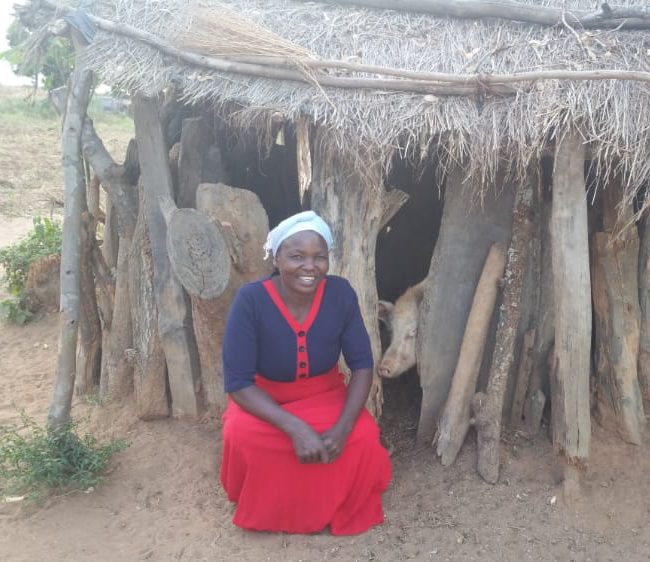 Bester Gondwe smiling and kneeling in front of her home